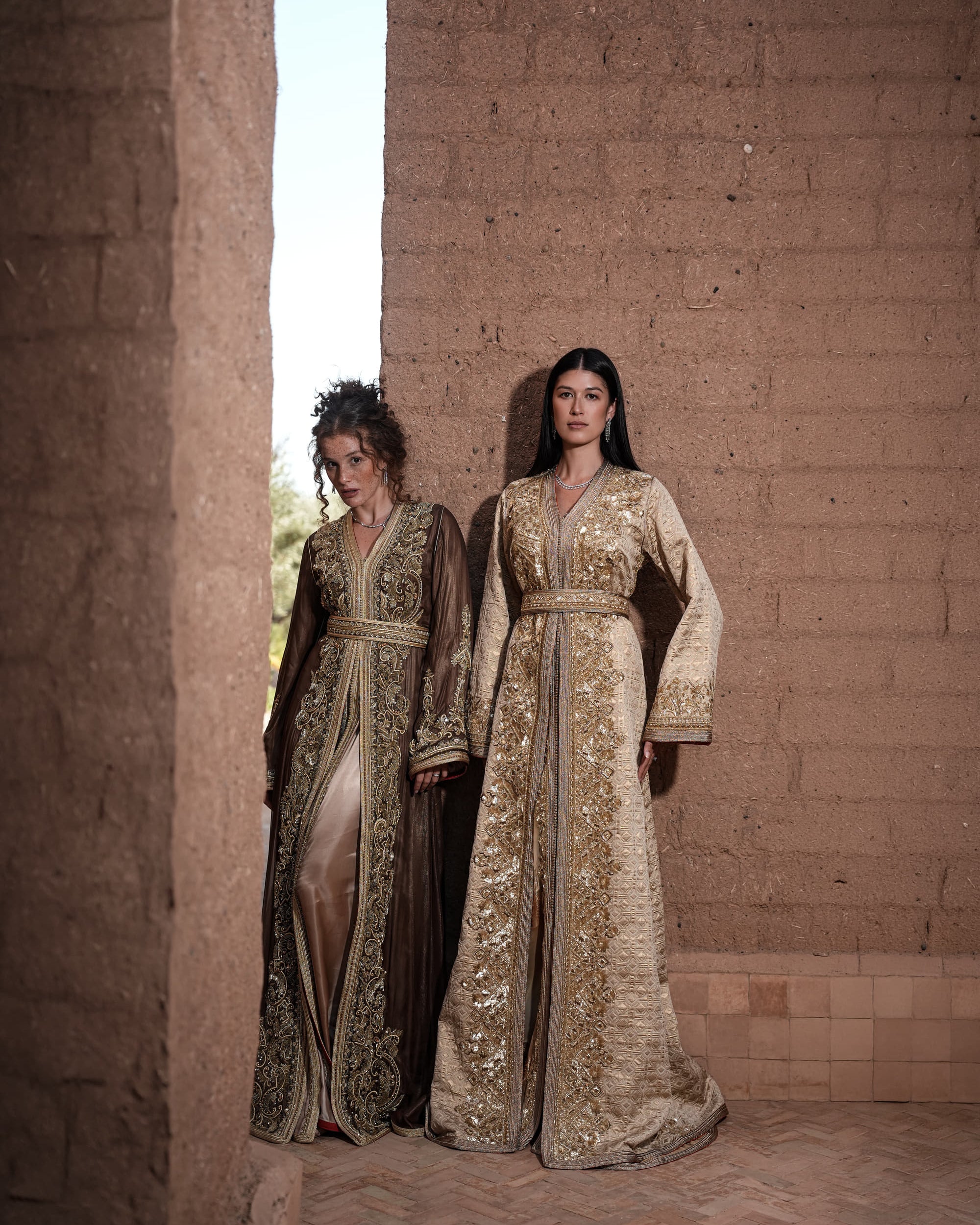 Bronze Reverie lamé organza Moroccan kaftan with gold embroidery, worn open over a champagne dress, shown alongside a second look